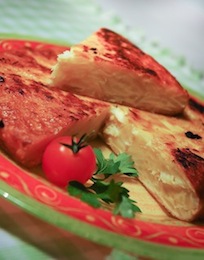 Punten Spaanse tortilla op een rood bord, met een tomaatje en peterselie